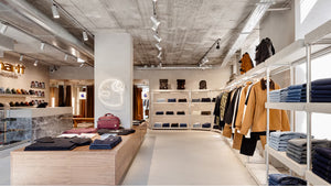 The image shows a modern retail store interior featuring Carhartt WIP clothing and accessories displayed on shelves and racks.