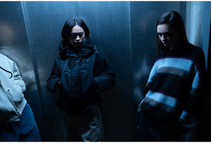 Three people stand in a dimly lit elevator, with one wearing a jacket featuring the Carhartt WIP logo.