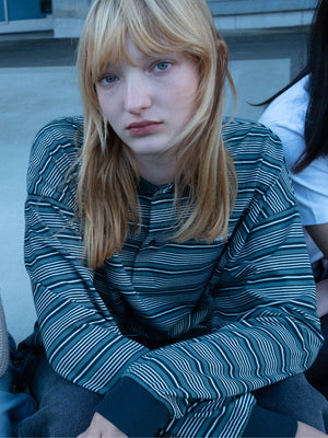 A person with long blonde hair is wearing a striped shirt, possibly from Carhartt WIP, sitting outdoors.
